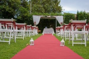 Ceremonia en el jardín del restaurante Priorat de Bayeres, con una alfombra roja, farolillos a los lados y sillas decoradas con lazos y flores rojas.