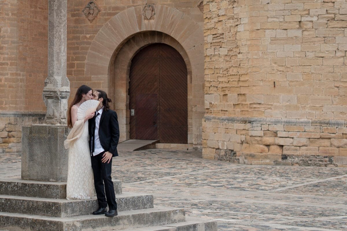 Beso tras un abanico ante una puerta en arco de Poblet